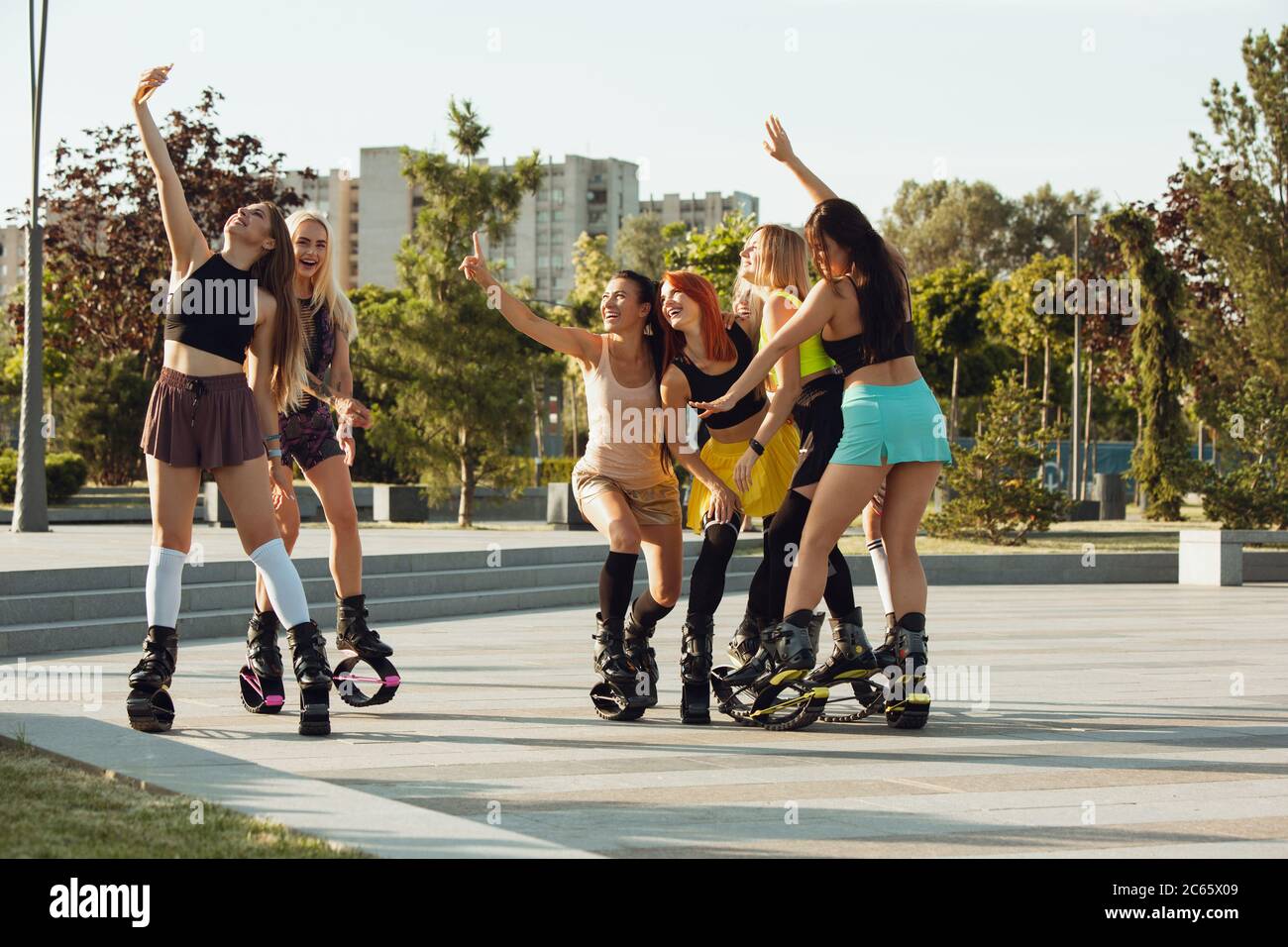 Close up women in sportswear jumping in a kangoo jumps shoes at the street  on summer's sunny day. Jumping high, active movement, action, fitness and  wellness. Fit female models during training. Photos