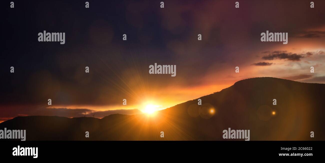 Sunset, sunrise over mountains. Sunbeams color the sky and the hills black silhouette. Sun and colorful sky background, card, wallpaper, panoramic vie Stock Photo