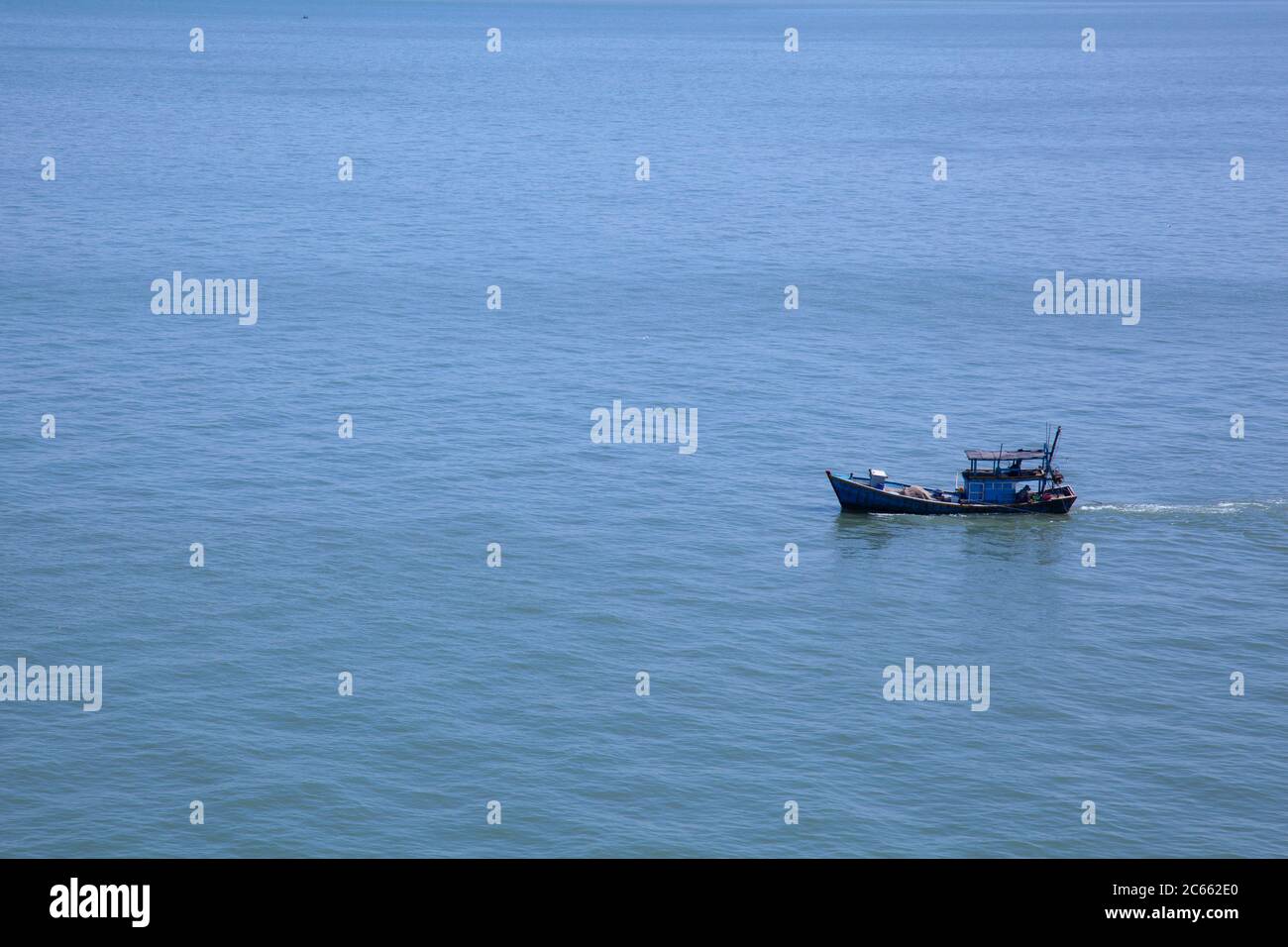 Solitary blue fishing boat on a vast calm sea with no other subject in the scene on the South China Sea near Vietnam. Stock Photo