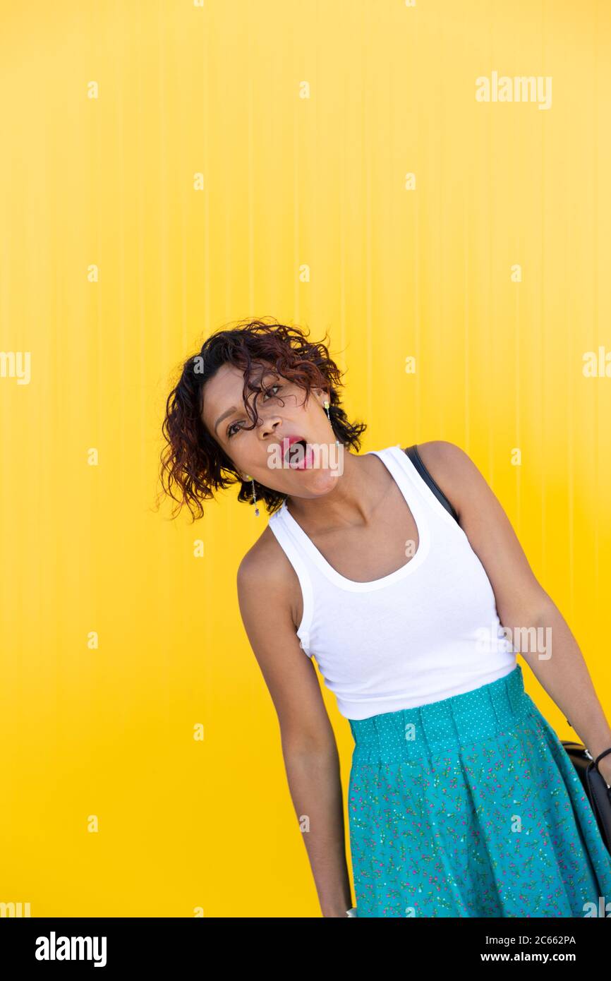 Brown-skinned girl in casual dress gesturing effusively on a yellow wall. Space for text. Expressions concept. Stock Photo