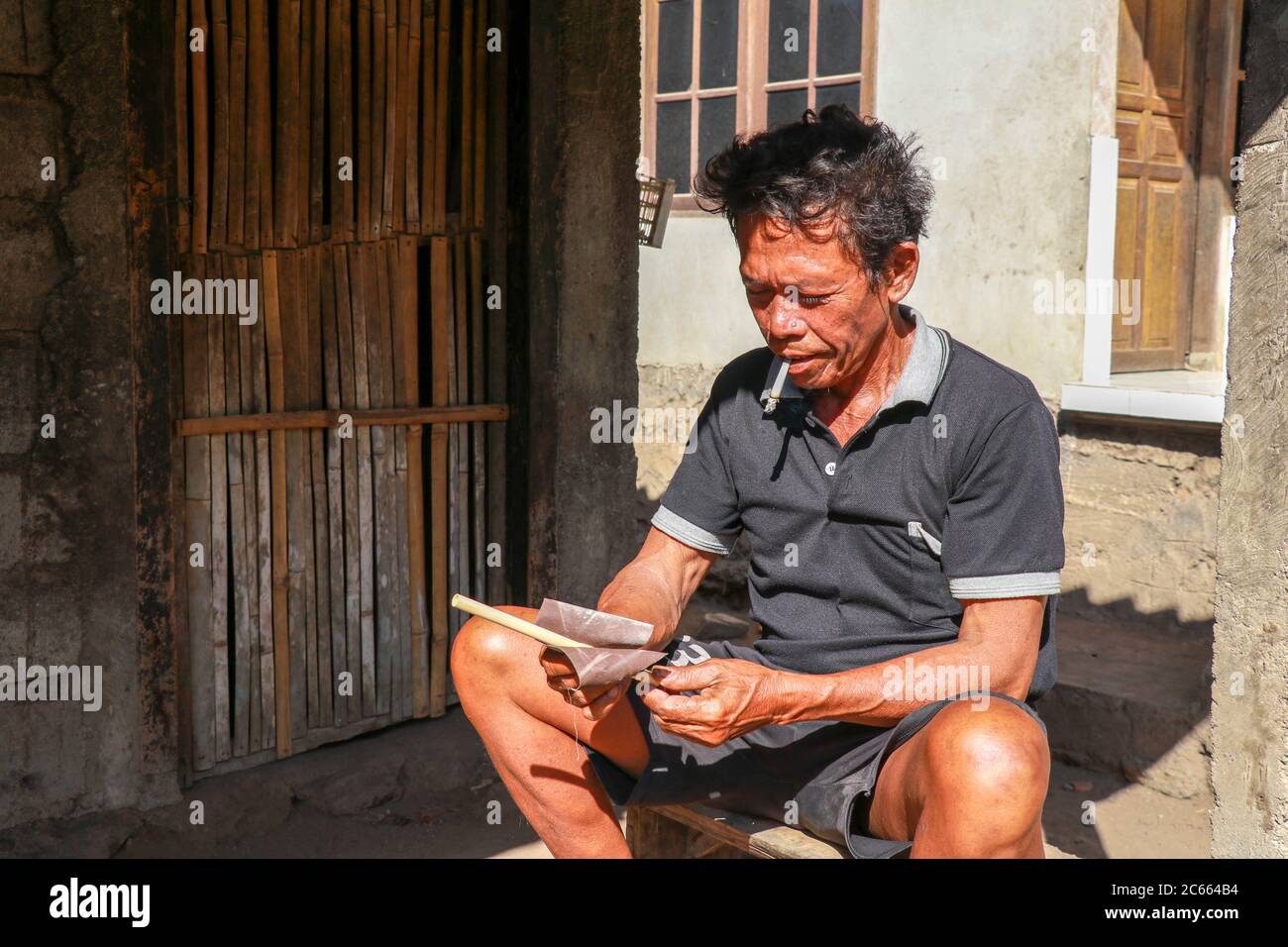 Old man working with bamboo in his workshop to make bamboo straws, Bali, Indonesia. Ecological way of producing recyclable products. Front view to a Stock Photo