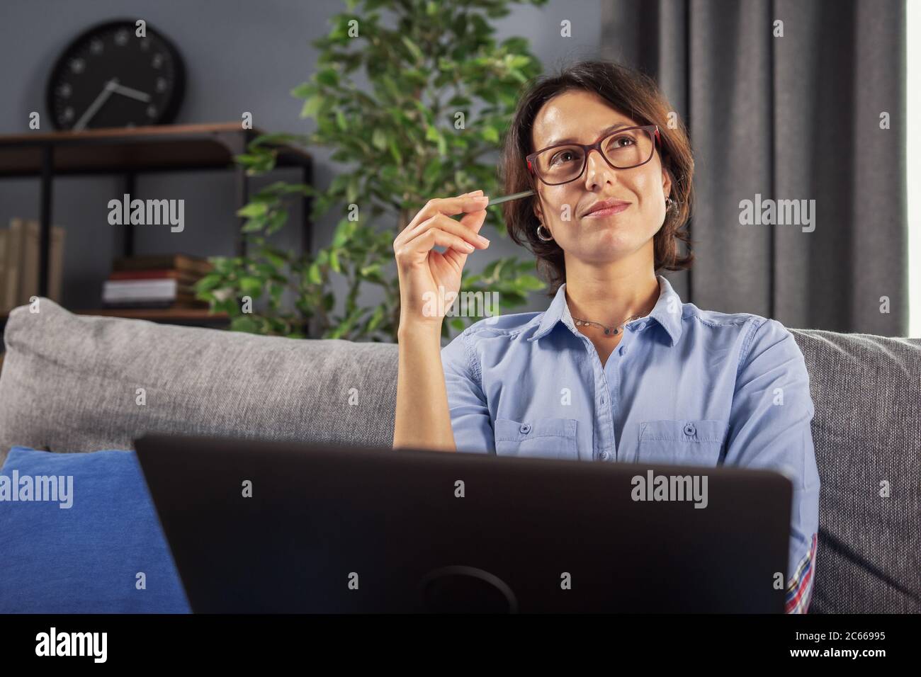 Lady sitting on sofa with laptop and looking for inspiration Stock Photo