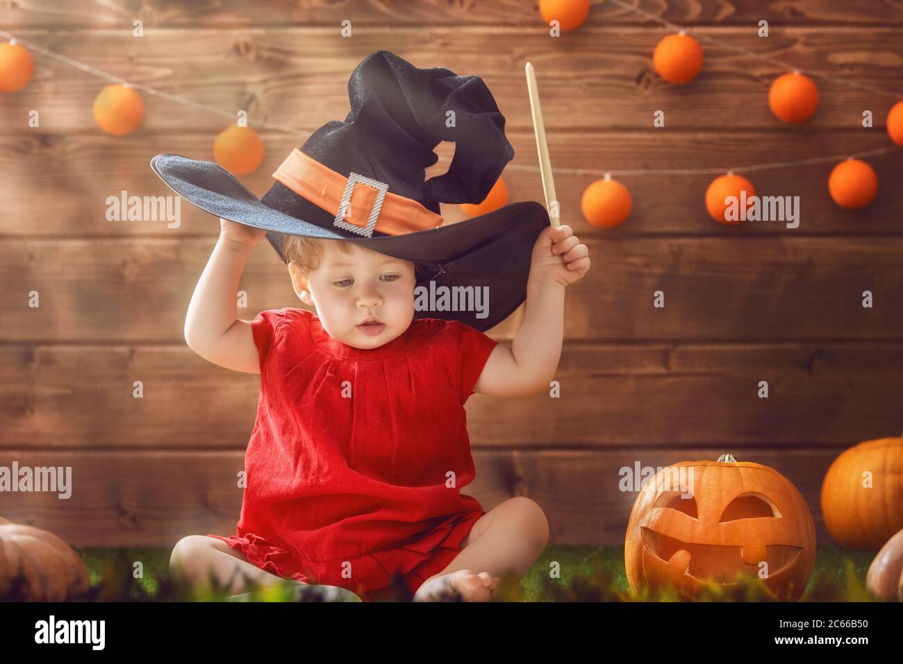 Happy Halloween! Cute cheerful little witch with a magic wand. Beautiful child  baby girl in witch costume sitting on grass Stock Photo - Alamy, image size:1300x957