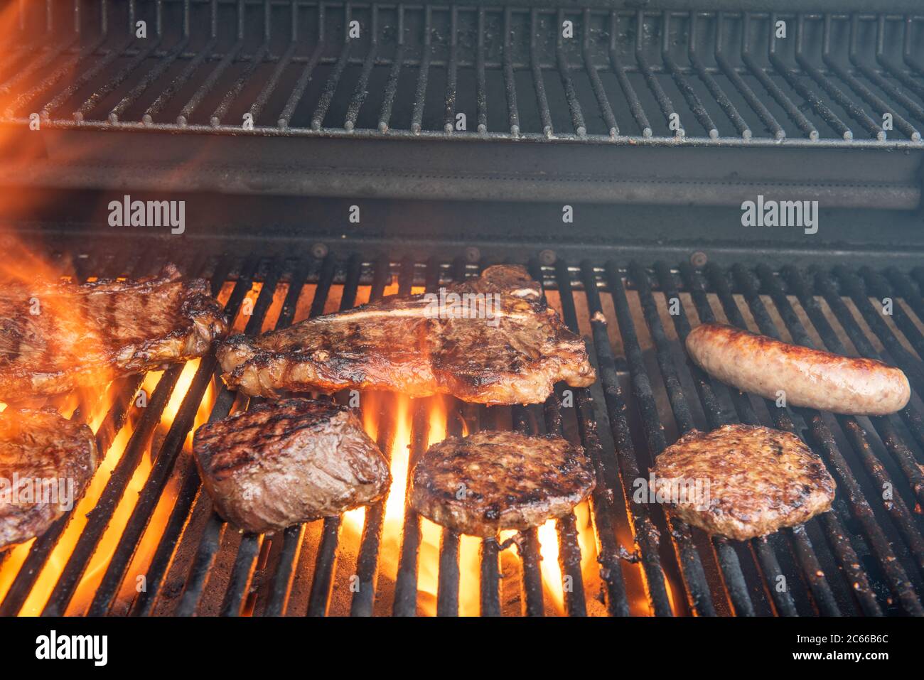 A grill full of different steaks including ribeye, T-bone, porterhouse, New York strip, Kansas city strip, filet mignon, plus hamburgers and brats wit Stock Photo