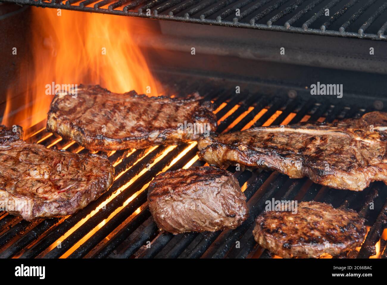 A grill full of different steaks including ribeye, Tbone, porterhouse