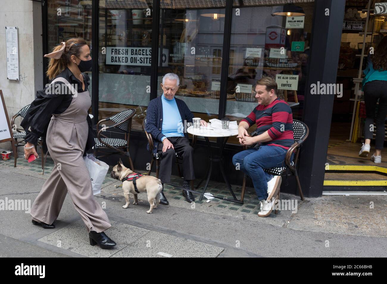 With the Coronavirus pandemic lockdown rules being eased, pubs and restaurant businesses are slowly re-opening and social distanced customers and their dog sit outside a cafe and people-watch on Wardour Street in Soho in the capital's West End, on 6th July 2020, in London, England. Stock Photo