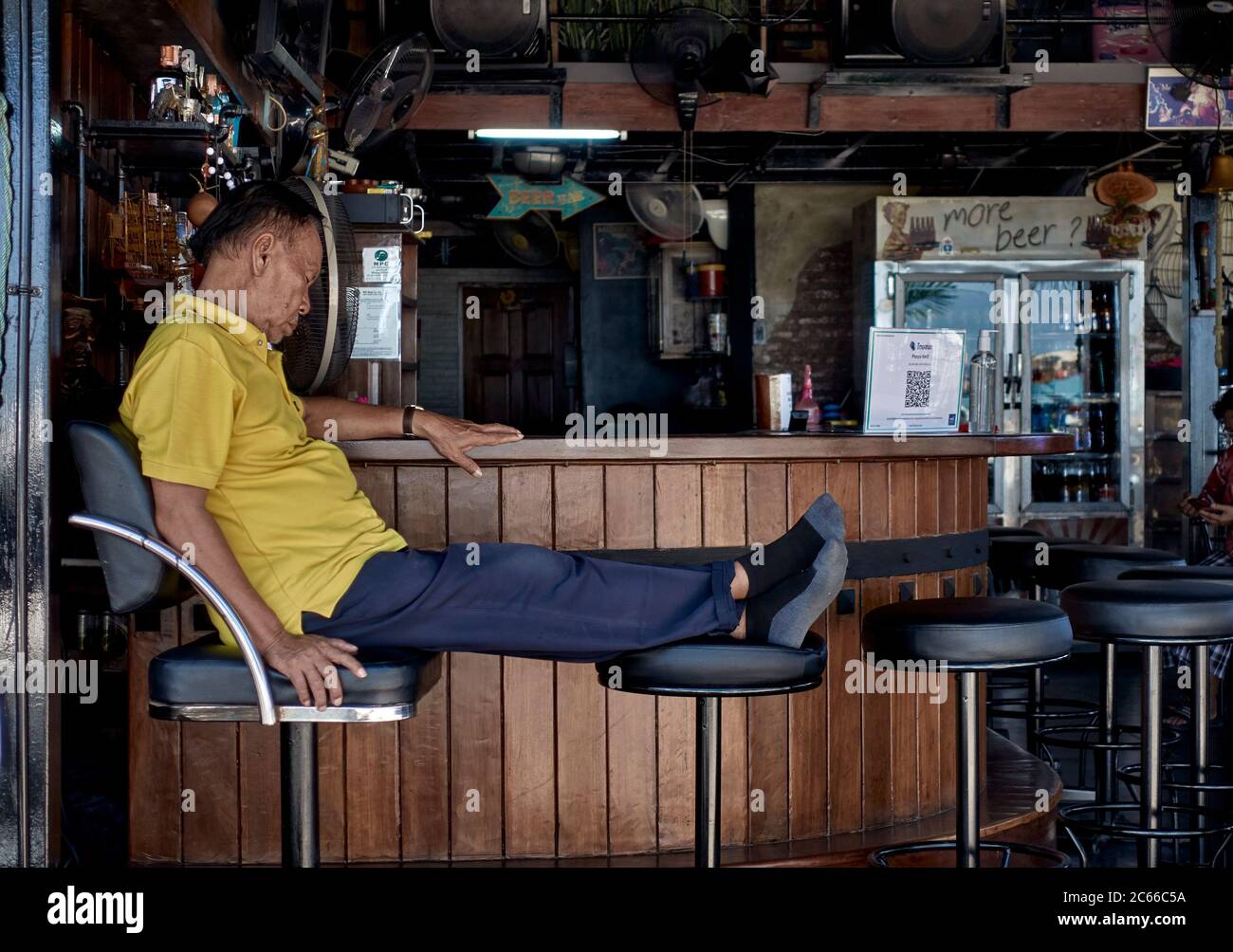 Concept Covid 19 virus lockdown and effect on business with owner asleep at his beer bar devoid of customers. Thailand Southeast Asia Stock Photo