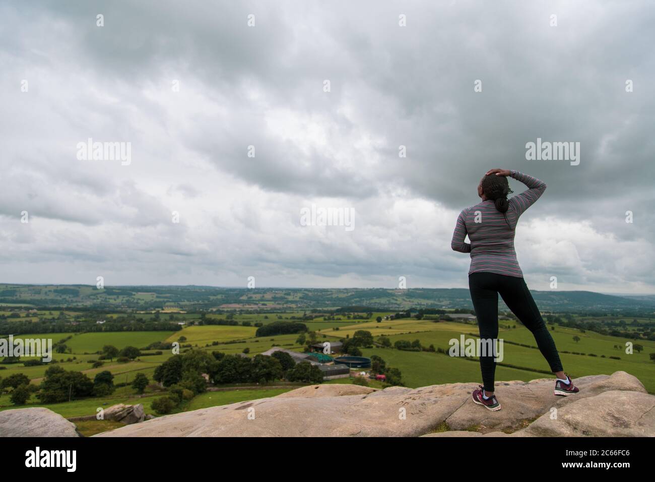 A black woman standing at the top of a rock looking at the cloudy horizon wearing athletic attire Stock Photo