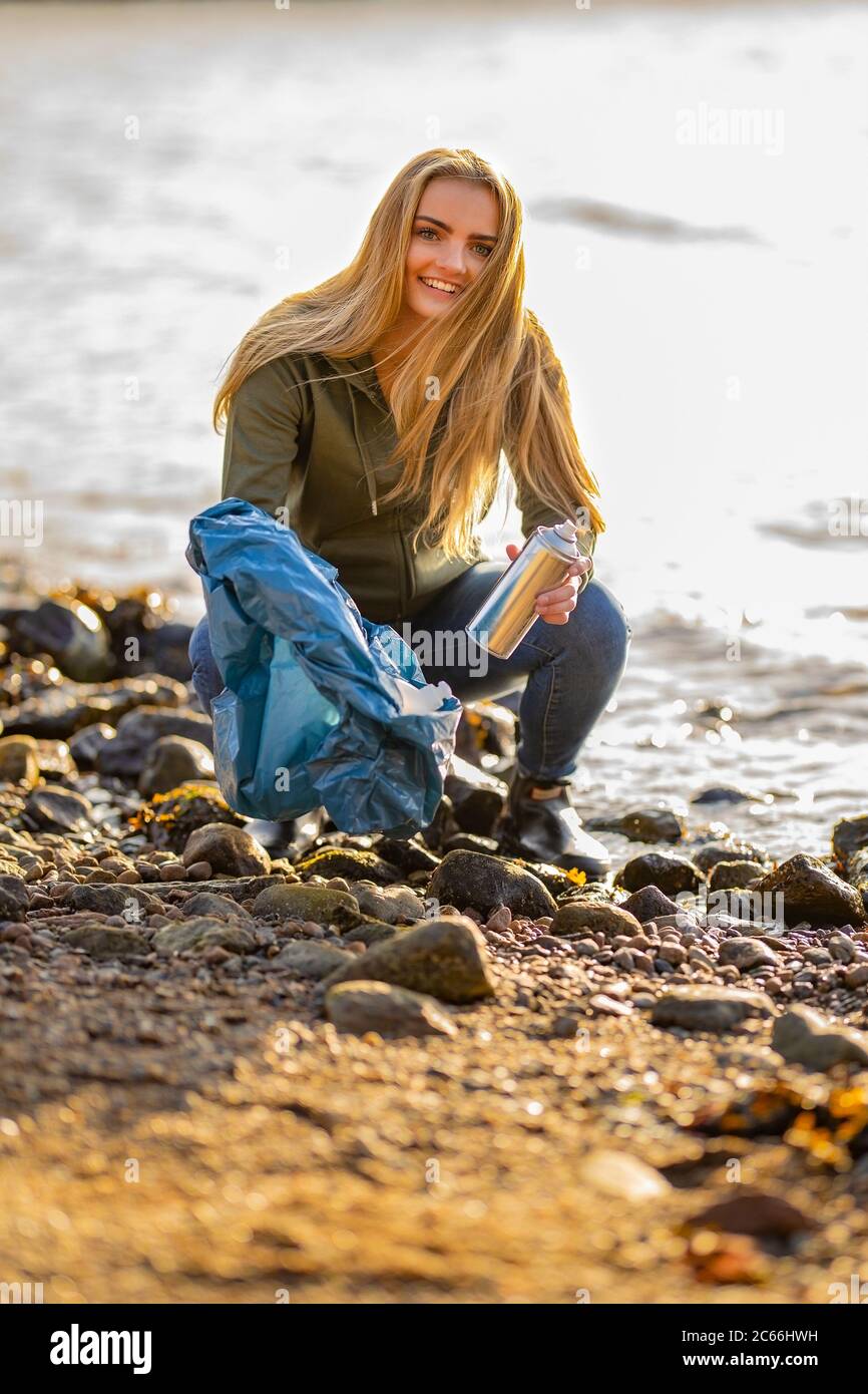 Young woman volunteer picking up aerosol can at beach Stock Photo