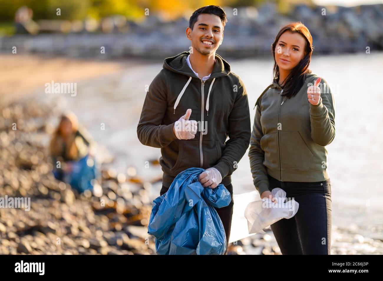 Young volunteers showing thumbs up at beach Stock Photo