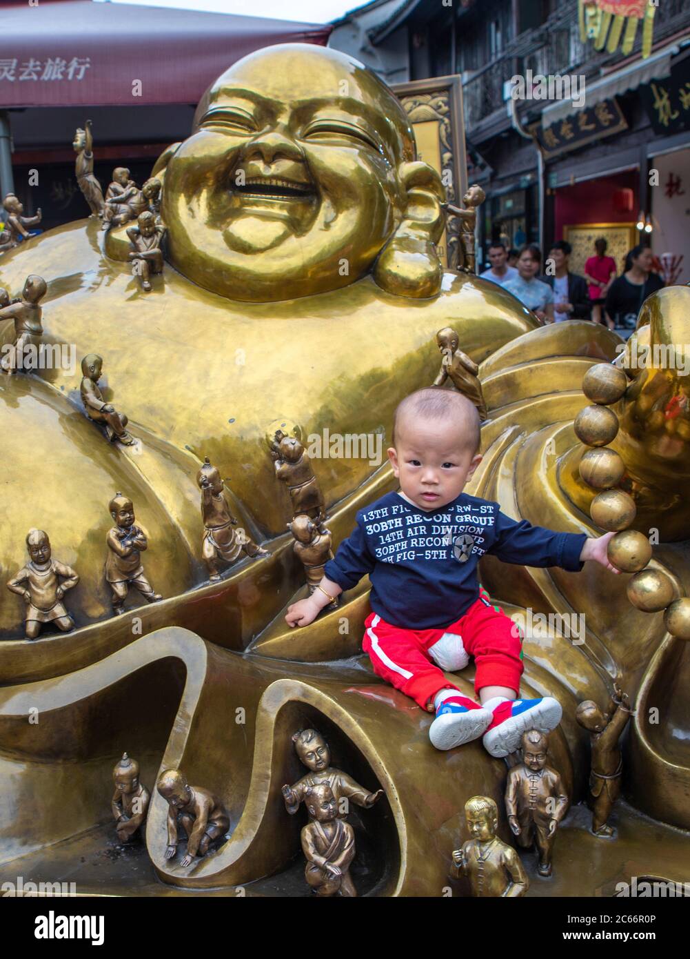 China, Hangzhou City, Hefang Street, child on golden Buddha statue Stock Photo