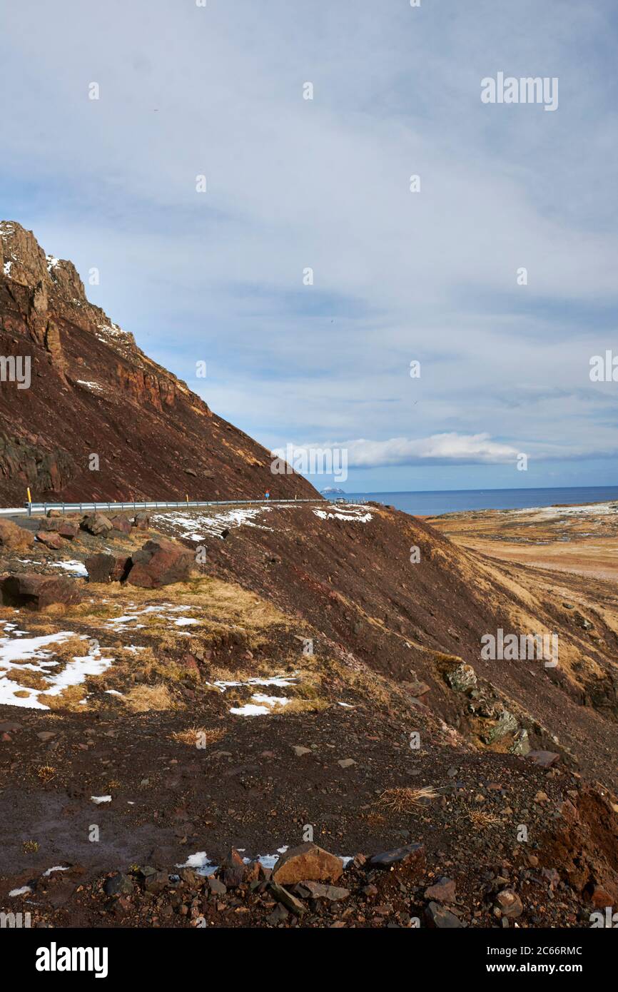 Iceland, windy road through the east Fjords, cloudy sky and snowcapped mountains i the distance Stock Photo