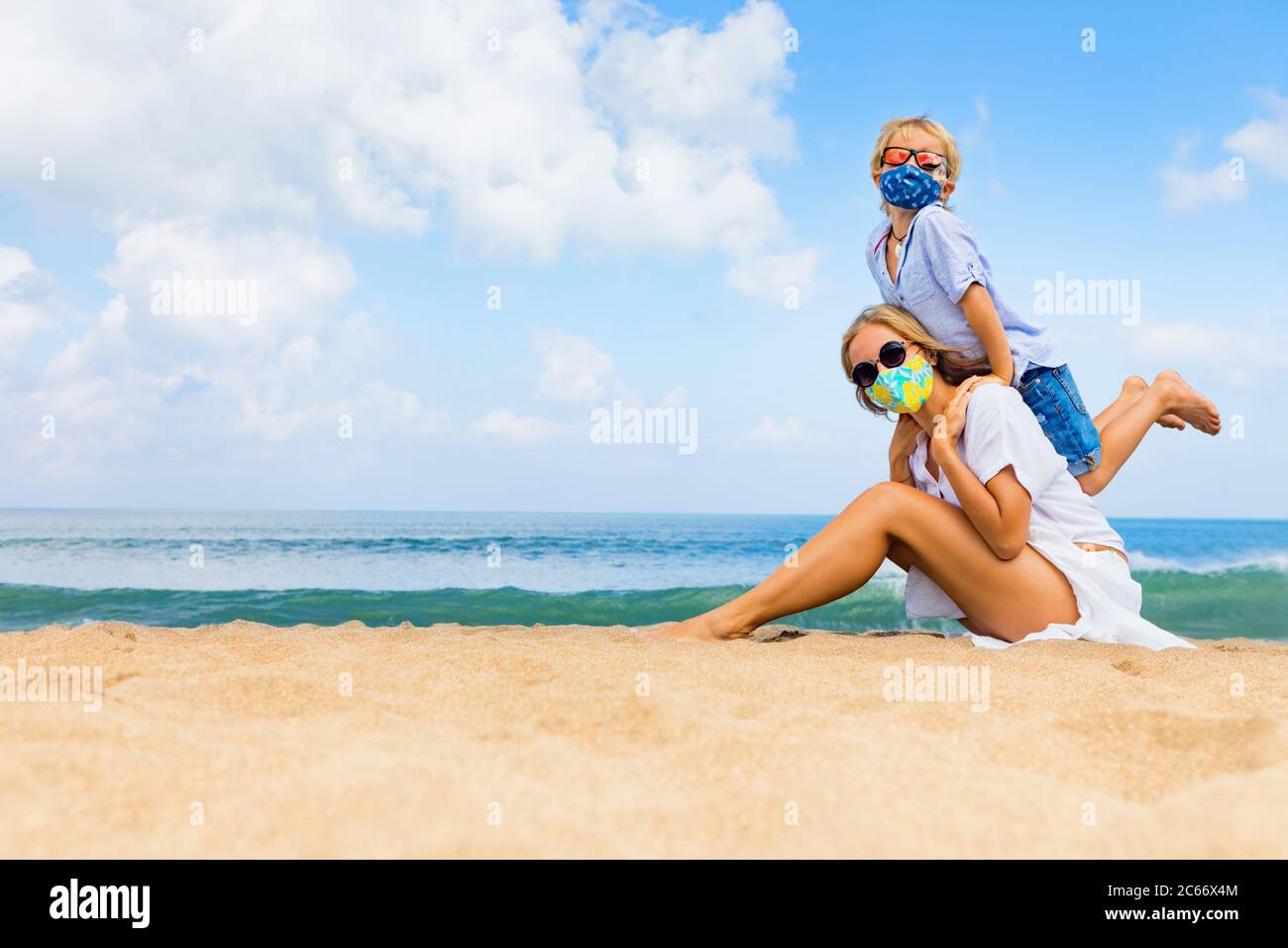Mother, child in masks have fun on sea beach. New rules to wear cloth face covering at public places. Cancelled cruise, tour due coronavirus COVID 19. Stock Photo