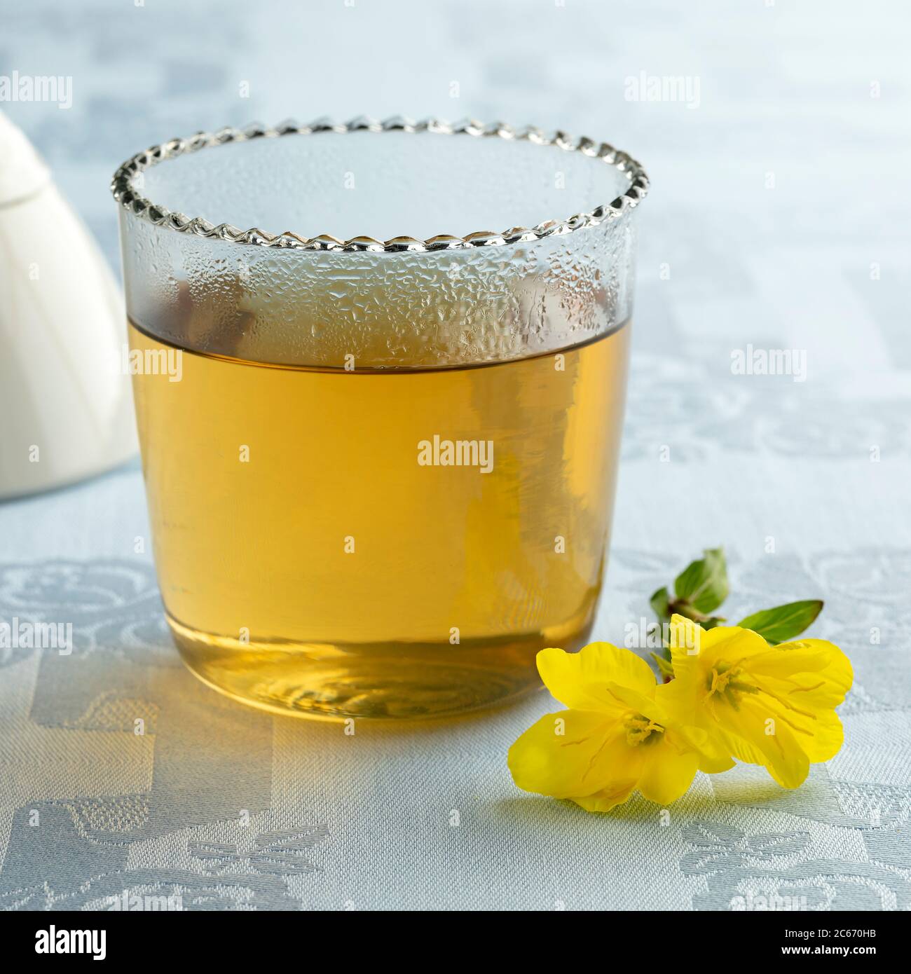 Glas cup with hot evening primrose tea and fresh yellow flowers Stock Photo