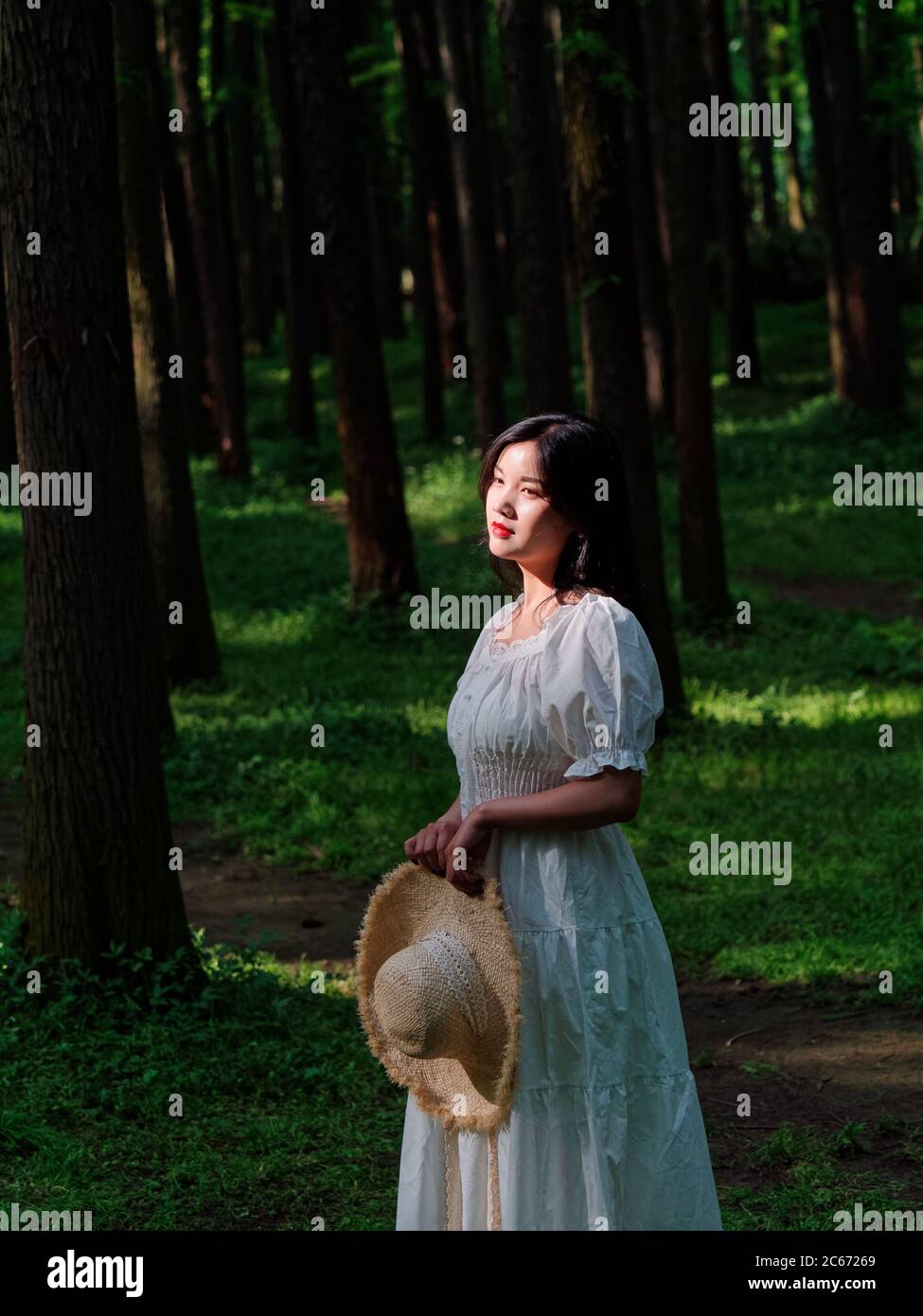 Portrait of Chinese girl in white dress stand in forest in sunny day Stock Photo