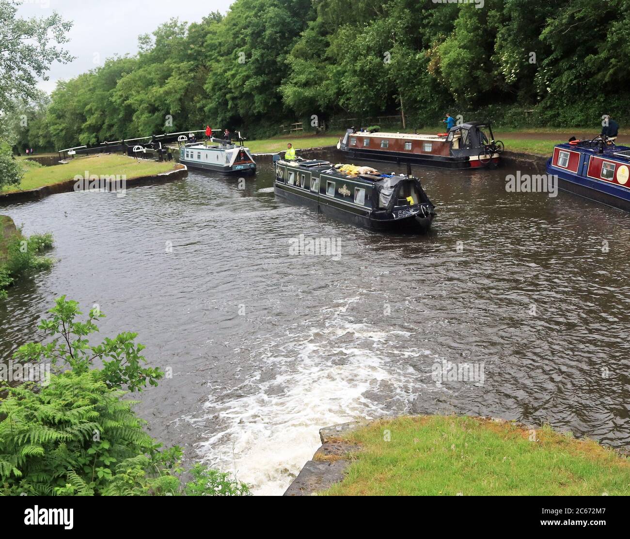 Four Narrow Boats working between Locks on the Wigan locks, two going up the flight leaving a lock and two down, with a good water flow. Stock Photo