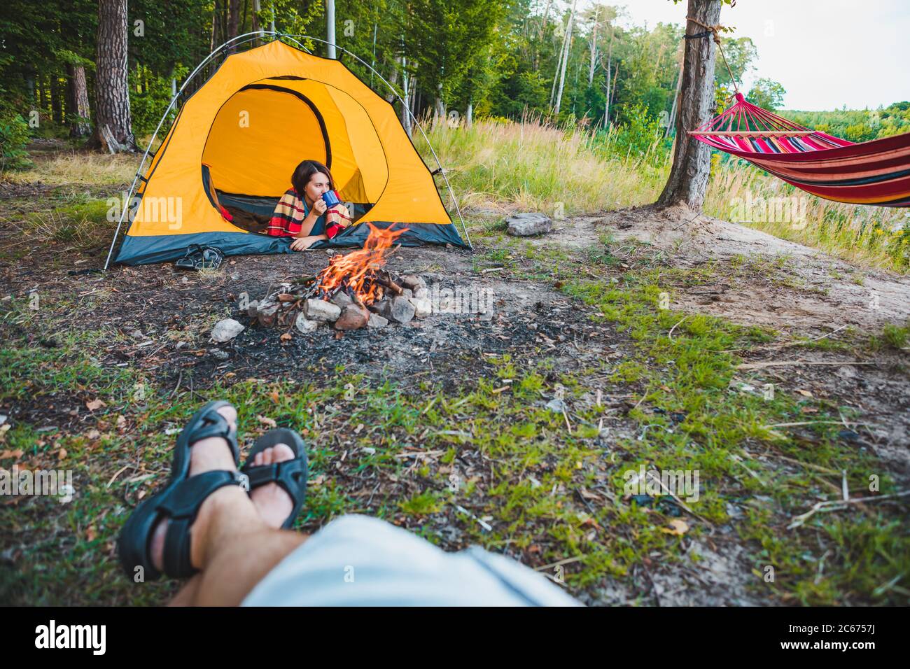 couple resting outdoors near cam fire in yellow tent Stock Photo