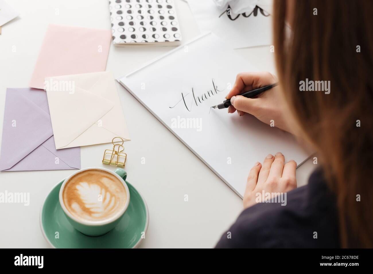 Beautiful photo of woman from backside sitting at white desk and writing notes isolated Stock Photo