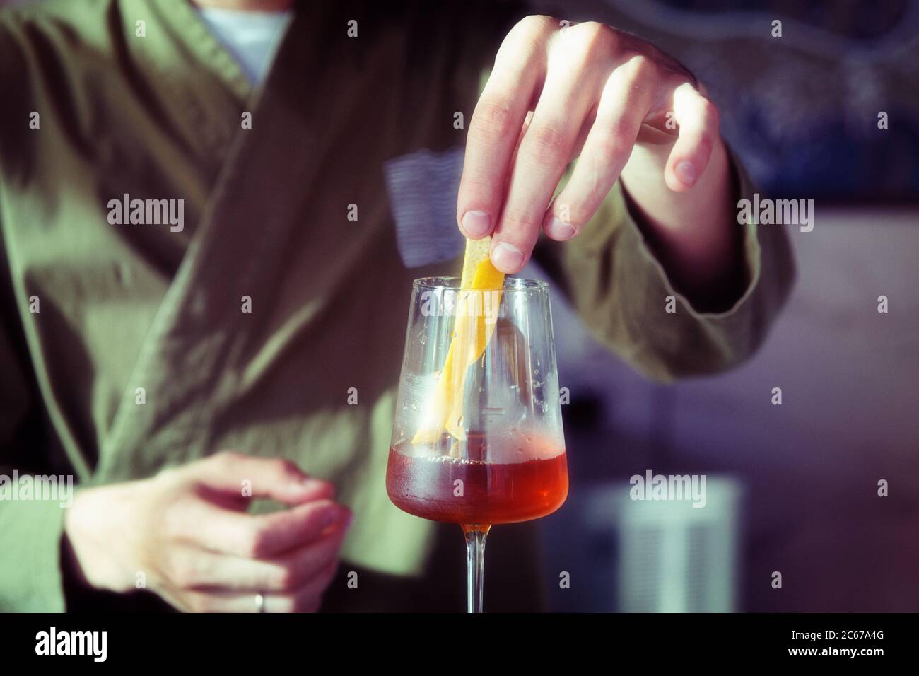 Male bartender is adding lemon zest to cocktail in wine glass, toned Stock Photo