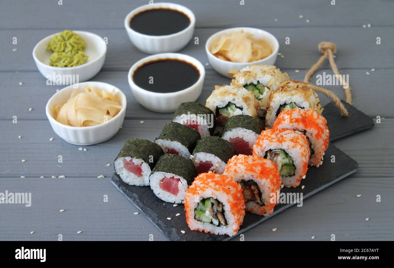 Various kinds of sushi rolls served on black stone and on gray wooden table. Japanese food side view Stock Photo