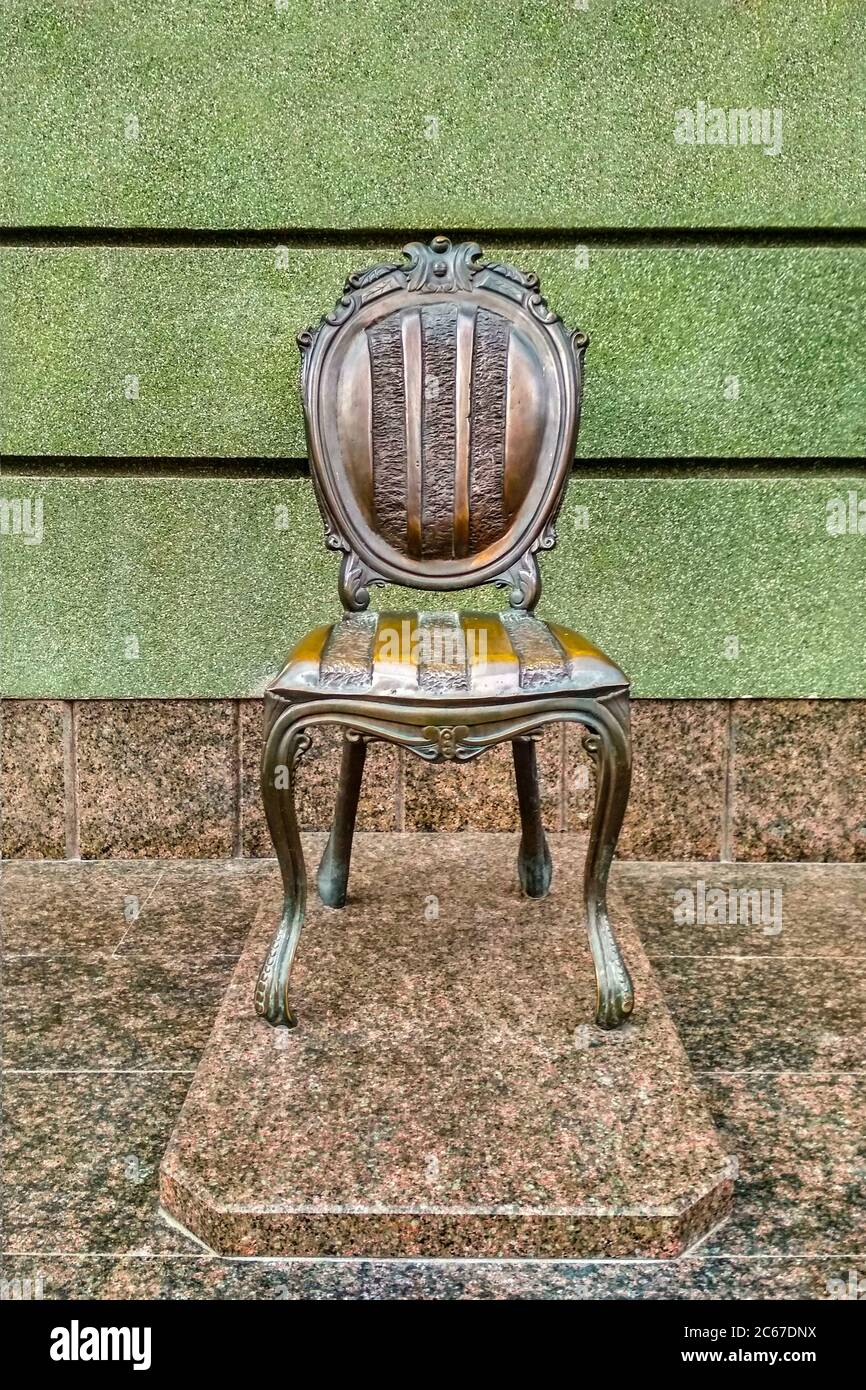 Bronze chair monument on a marble pedestal against the background at the green wall Stock Photo