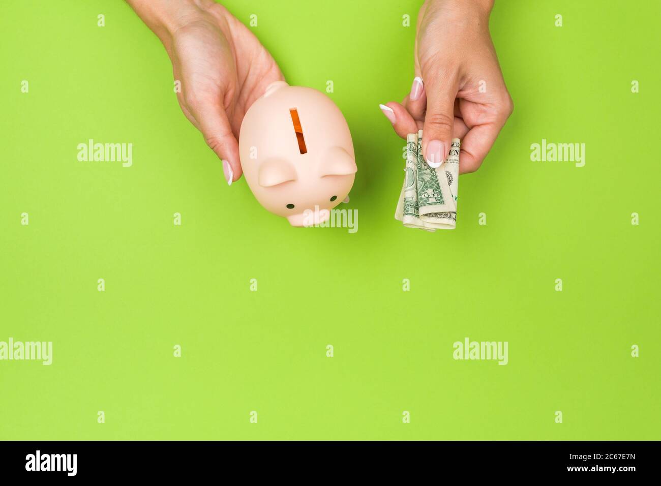 female hands put money in a piggy bank on a green background. Savings