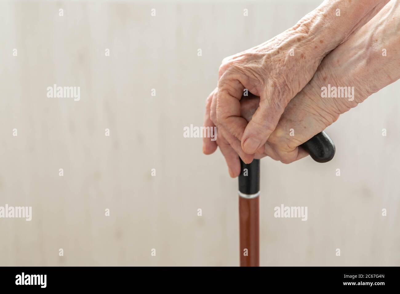 Elderly hands resting on stick. Close up hands of old woman holding walking stick. Hands of woman pensioner on a walking stick closeup. Old lady holdi Stock Photo