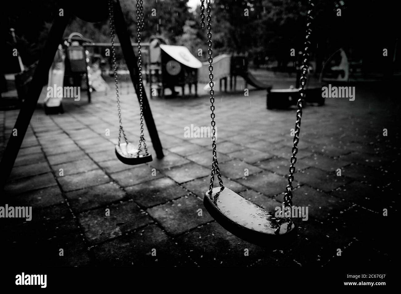 Plastic and wet swings in an empty playground during a rainy summer day. Stock Photo