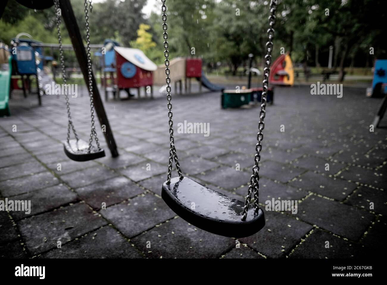 Plastic and wet swings in an empty playground during a rainy summer day. Stock Photo