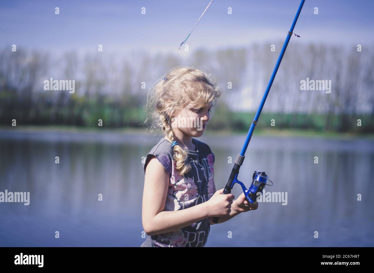 Little blond girl with straw hat prepares her fishing rod sitting near the  lake Stock Photo - Alamy