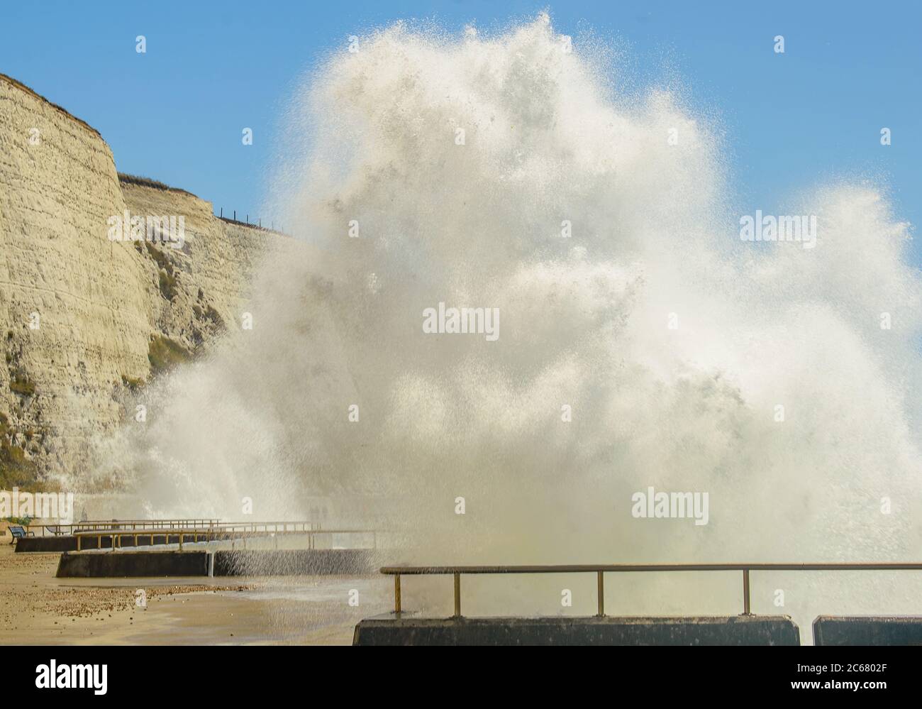 Close by the towering white foamy waves crashing onto the seafront walkway next to the white cliffs Stock Photo