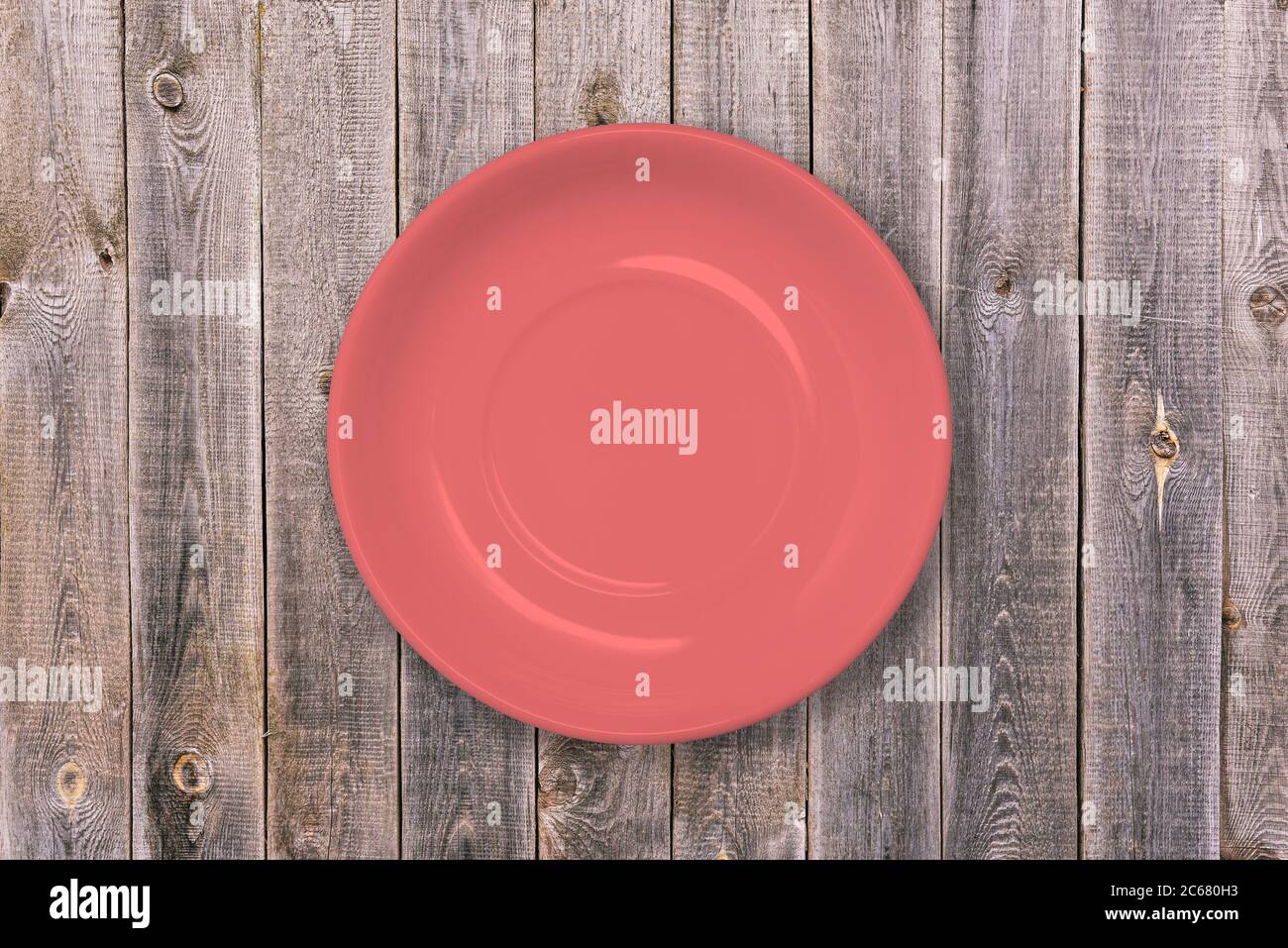 Plate on a wooden table. Red empty food plate. A dish for Breakfast, lunch and dinner. Tableware for home and restaurant. Concept of food and cooking Stock Photo