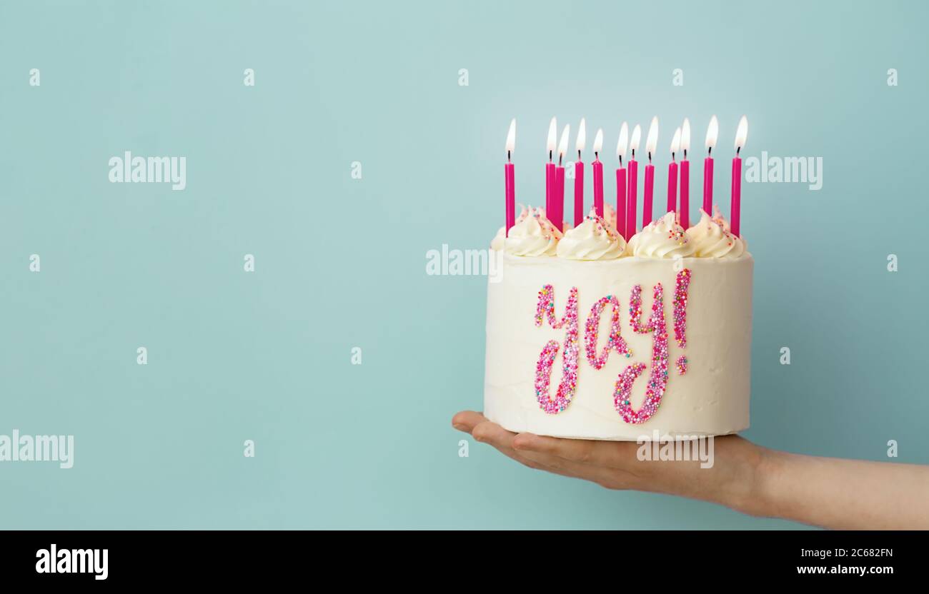 Hand holding birthday cake with pink candles and yay written in