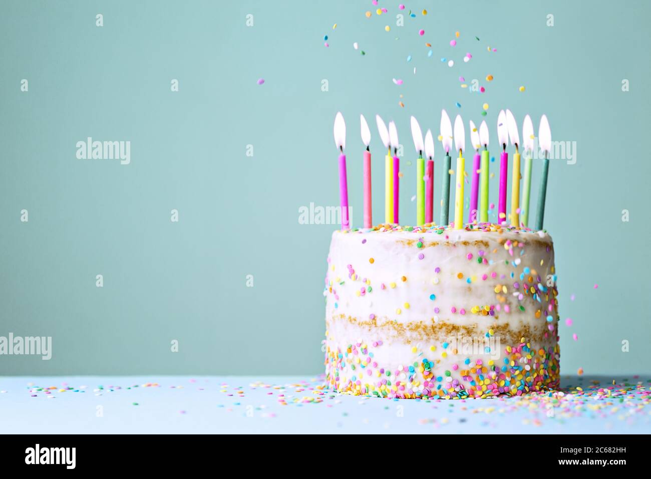 Naked funfetti birthday cake with colorful candles and falling sprinkles Stock Photo