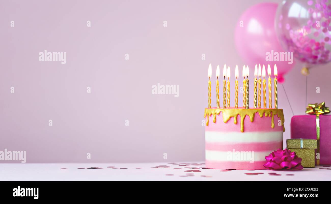 Pink birthday cake with golden candles and balloons Stock Photo