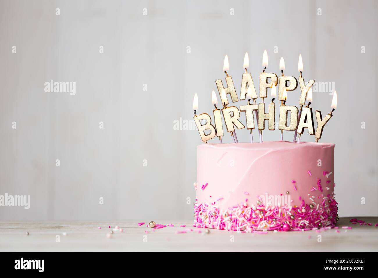 Pink birthday cake with gold happy birthday candles Stock Photo