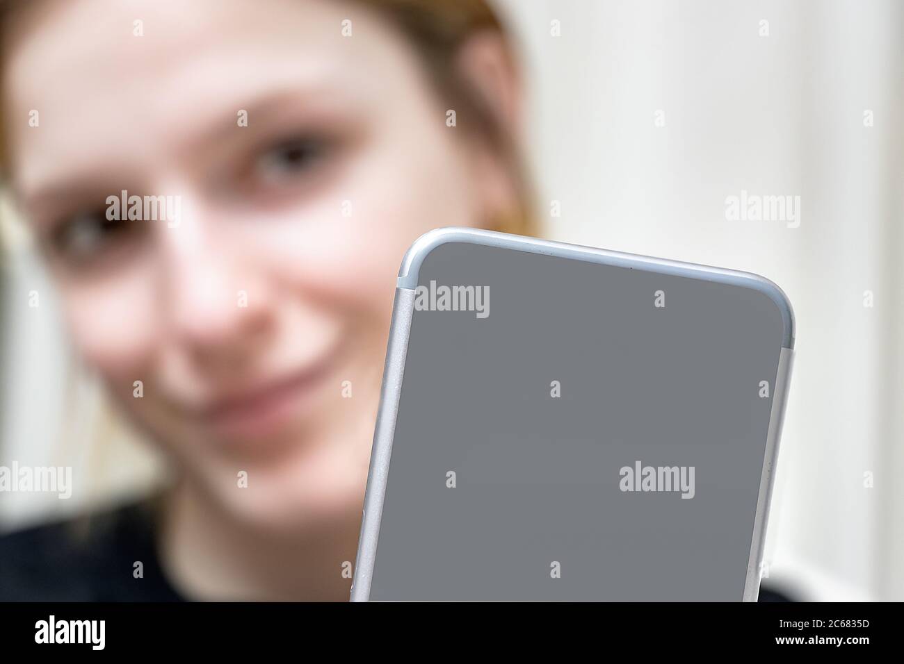 Blurred girl taking a selfie photo with her smartphone at home. Close up of the back of a mobile phone. Stock Photo