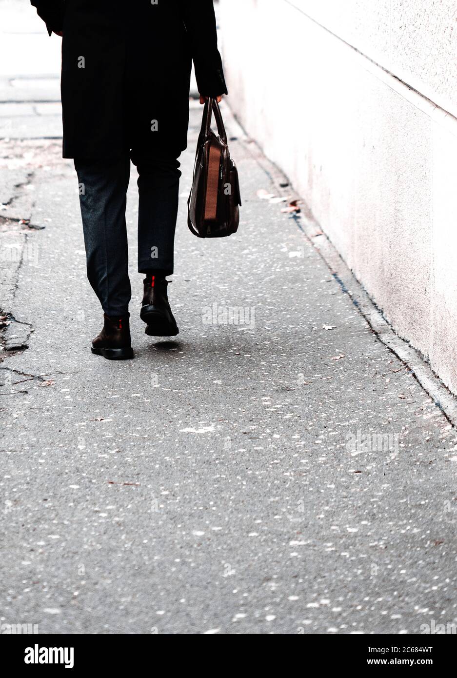 Man walking on sidewalk carrying a bag Stock Photo