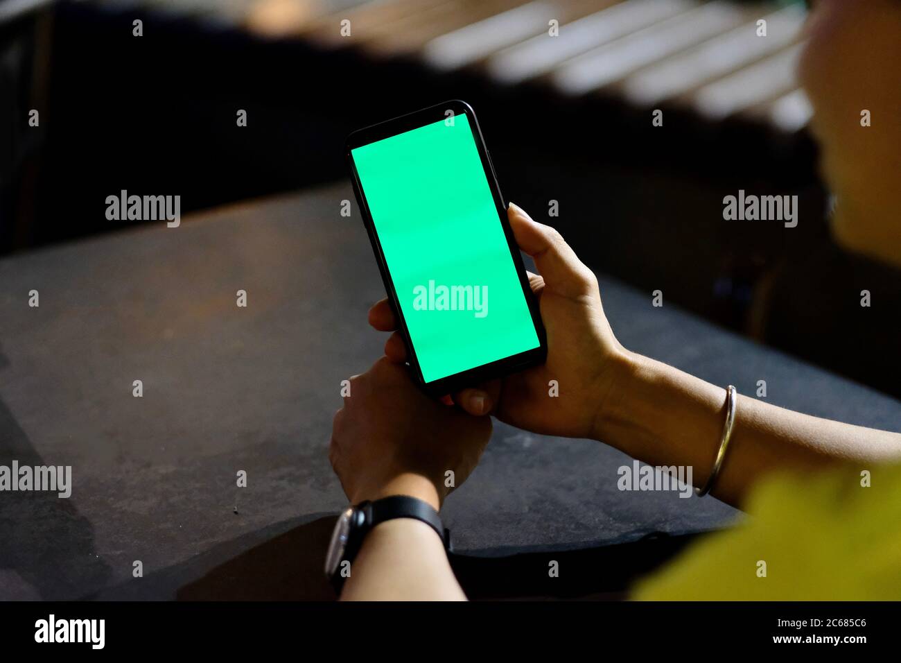 Over shoulder view of young man looking at green screen smartphone outdoor at night. Blur background Stock Photo