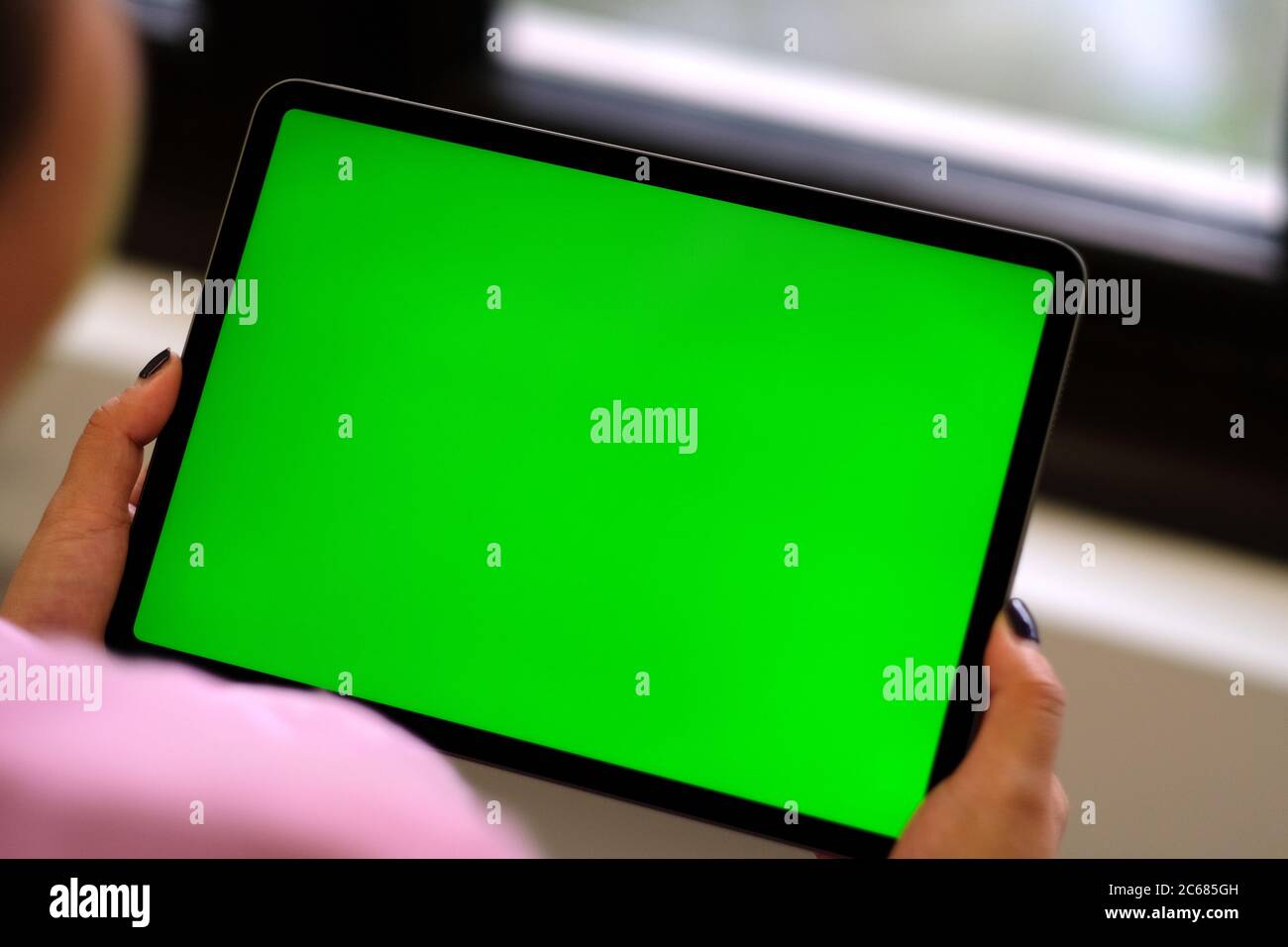 Over shoulder of woman holding green screen tablet device near window