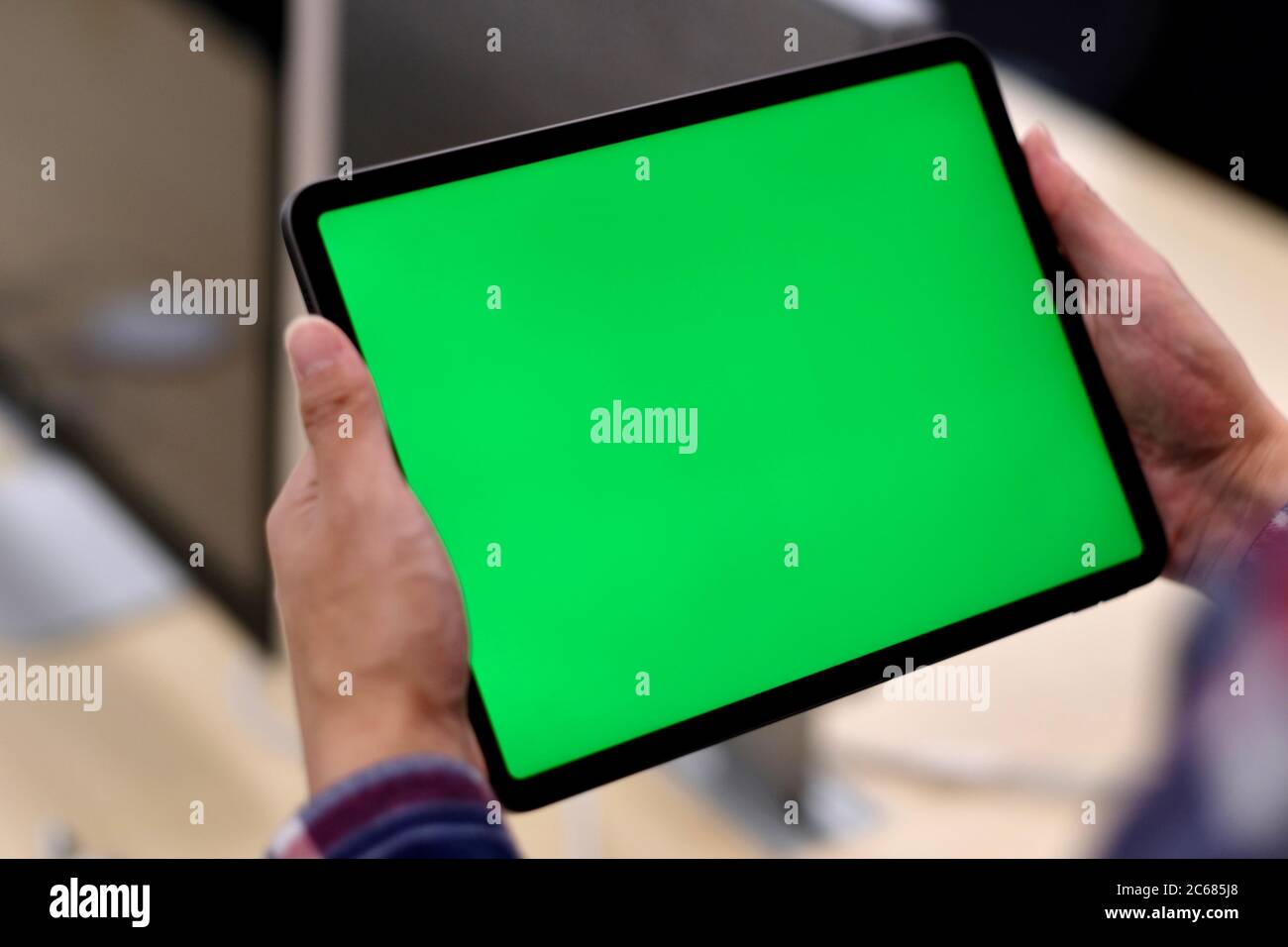 Over shoulder of man holding green screen tablet in office. Blur background Stock Photo