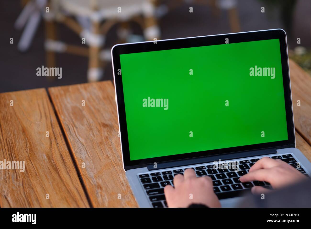 over shoulder of people using green screen laptop computer on wooden table. blur background Stock Photo