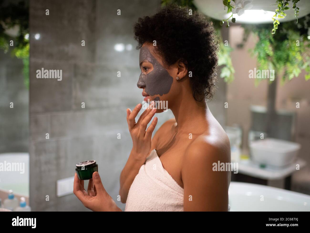 Side view of black female applying mud mask on face during skin care routine at home Stock Photo