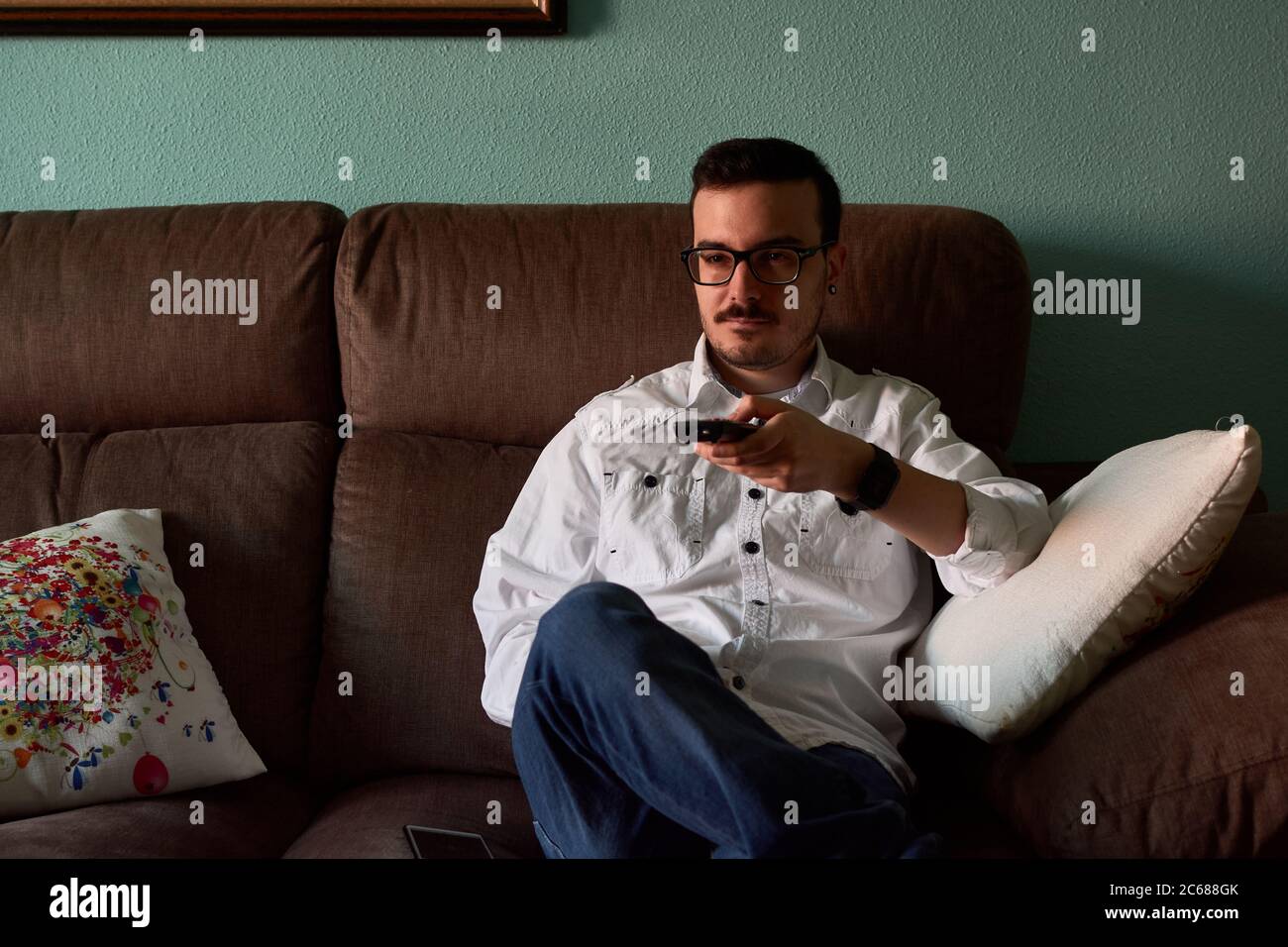 Young man changes channels with his remote control at home Stock Photo