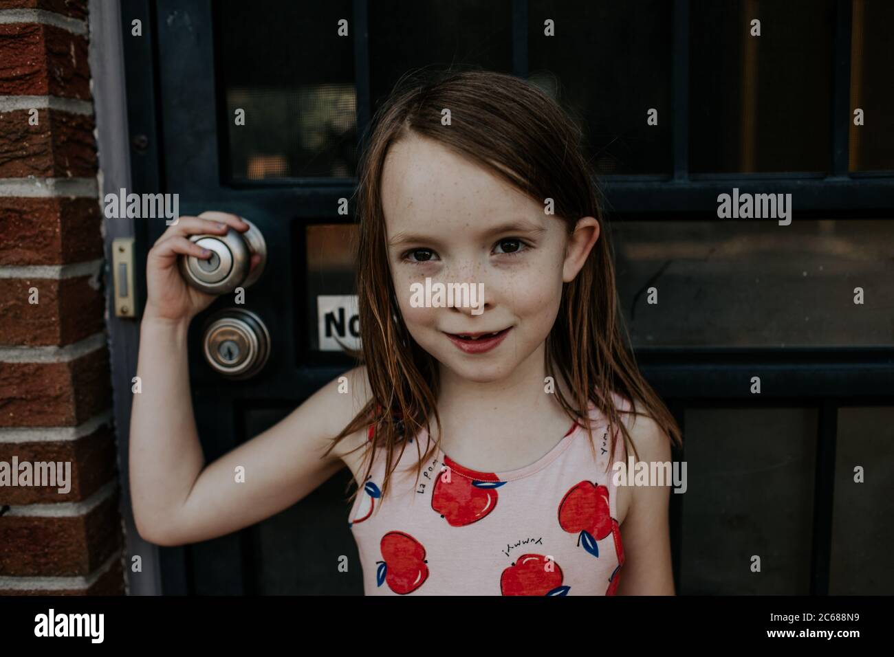 Happy young girl standing outside front door smirking Stock Photo - Alamy