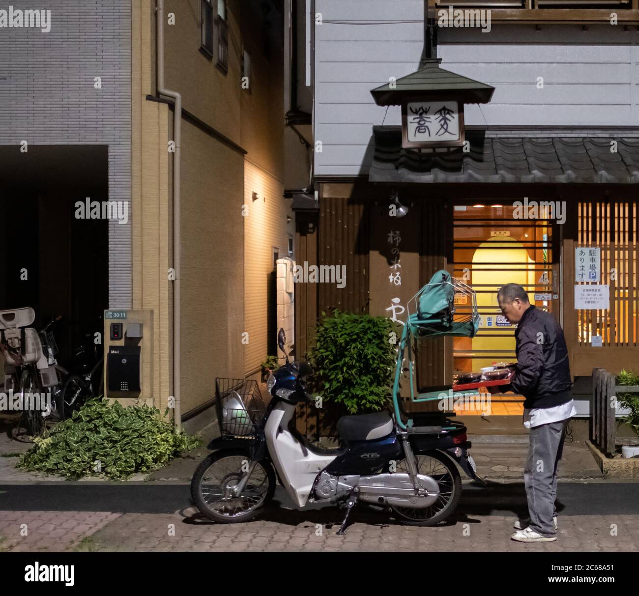 Elderly food deliveryman in Kamimeguro street, Tokyo, Japan at night. Stock Photo