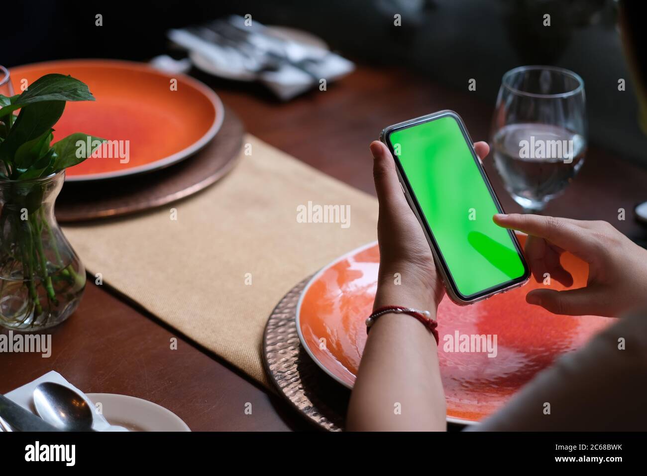 over shoulder of people tapping green screen smartphone in restaurant. blurred plates and drinking glass on table. Stock Photo