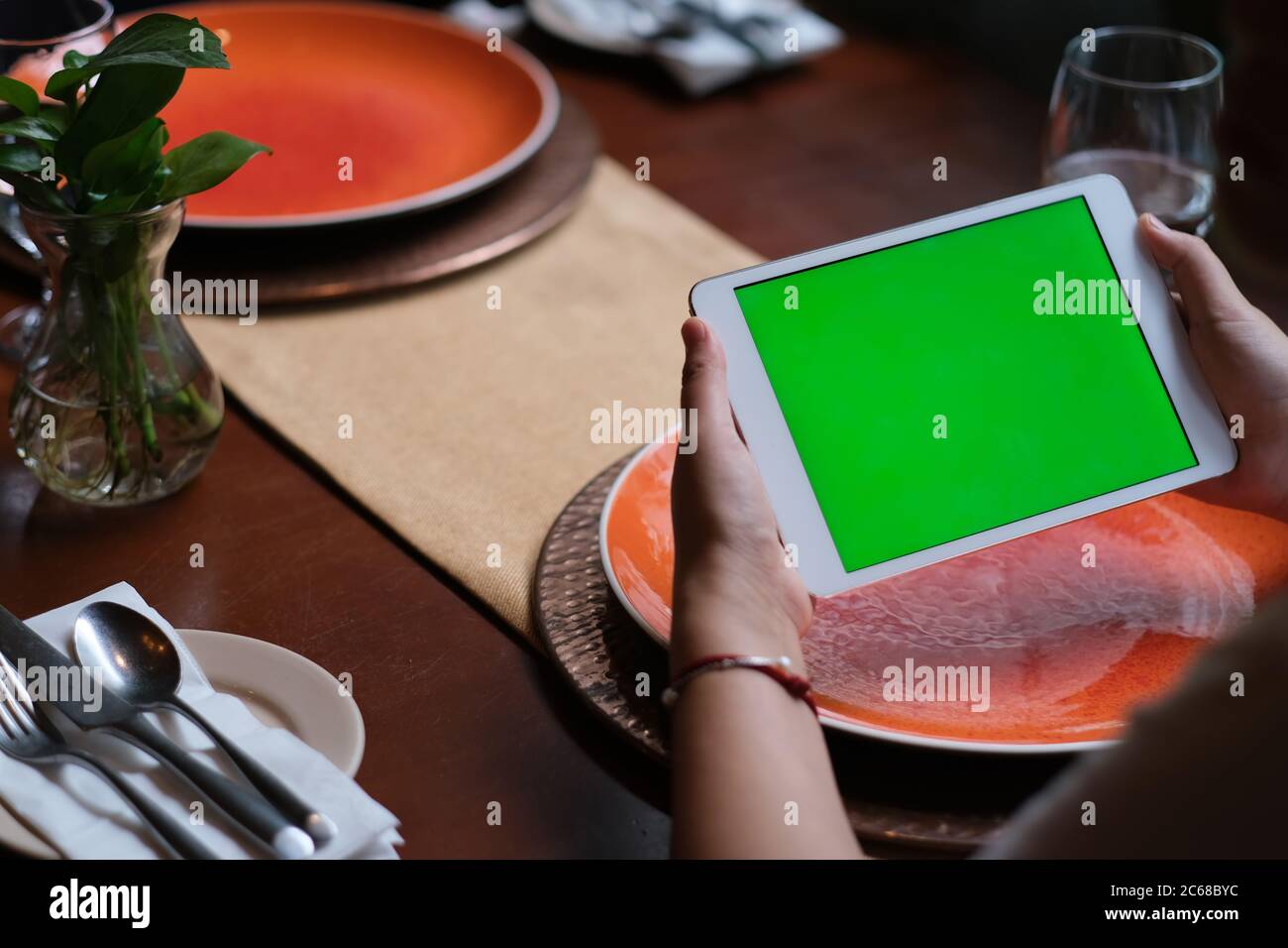 over shoulder of people using green screen tablet in restaurant. blurred plates on dining table. Stock Photo