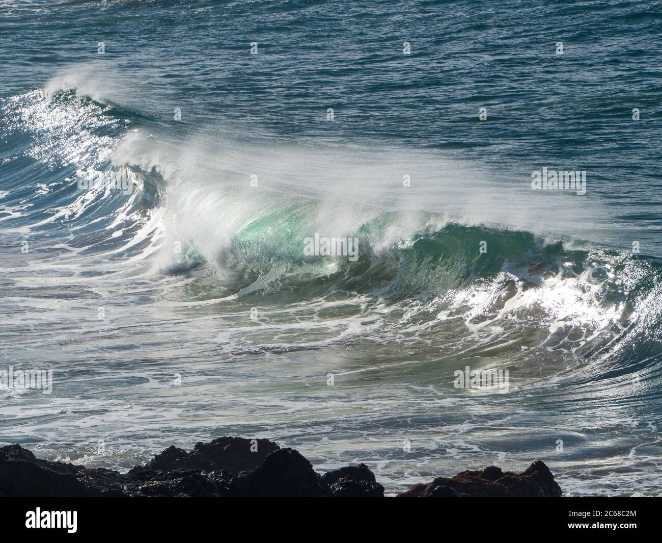 A shiny glassy blue green wave breaking and rolling over with spray ...