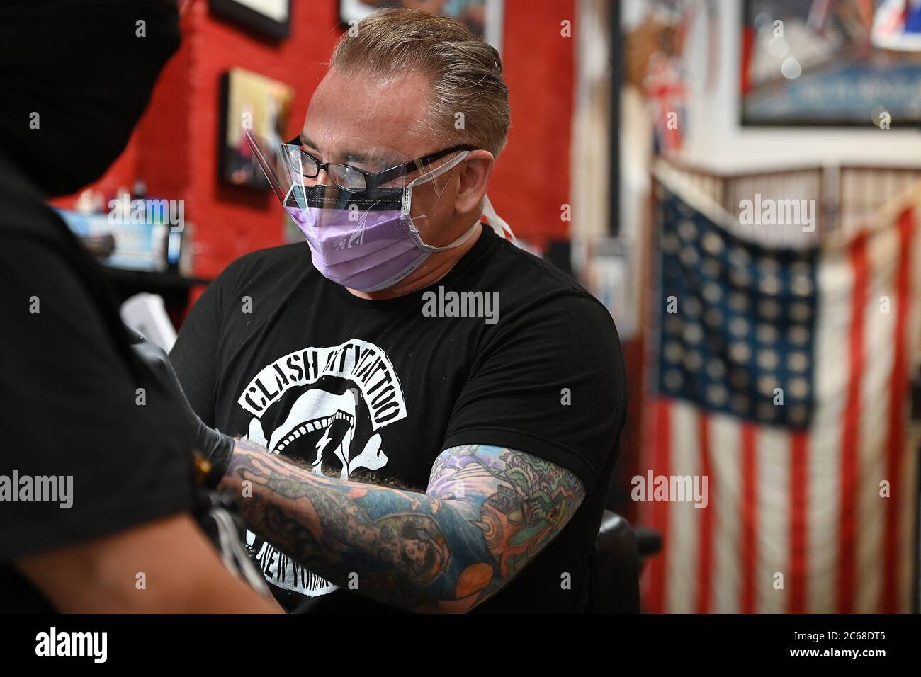 New York City, USA. 07th July, 2020. Both wearing a mask in the time of  COVID-19, shop owner and tattoo artist Barry Shailes presses ink into the  skin of Javier Malave, at